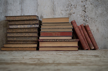 libri antichi appoggiati in verticale e orizzontali su tavolo legno e muro grezzo