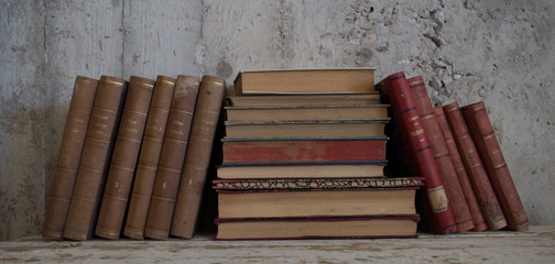 libri antichi appoggiati in verticale e orizzontali su tavolo legno e muro grezzo