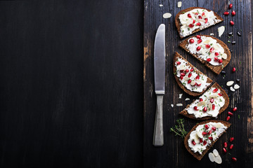 Open sandwiches rye bread with cream cheese and pomegranate seeds, flakes of almond  on marble surface. Healthy snack concept. Top view.