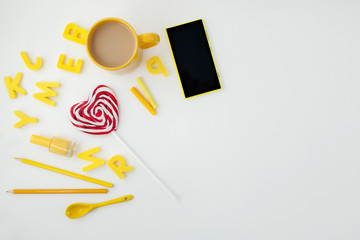 yellow cup, heart shaped candy, letters ,yellow phone and pencils on white background. Place for text. View from above