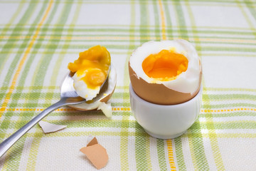 Boiled fresh smash broken egg for the breakfast on the porcelain stand for eggs. Broken beige hen egg and pieces of shells, bright liquid orange yolk in the spoon.