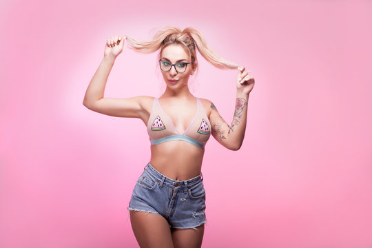 Hot sexy blonde woman in swimsuit and short jeans on pink background in studio photo