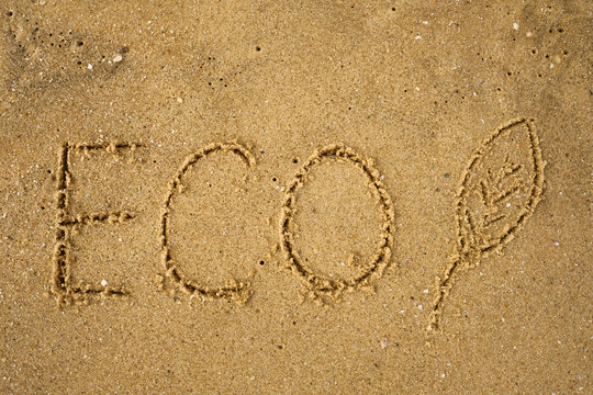 Word ECO frawn on sandy yellow beach. Concept of eco safe lifestyle