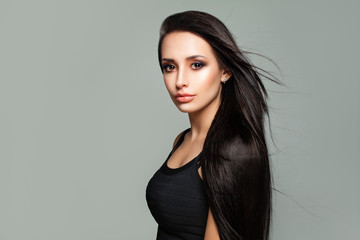 Young Brunette Woman with Shiny Blowing Hair and Natural Makeup on Gray Background