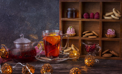 on a wooden table tea in a kettle, a mug with tea and sweets: cookies, cakes, berries, honey