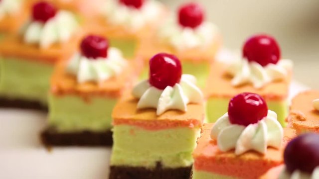 Closeup view of many small cakes served on table for cocktail party or on shelves at store. Pastries decorated with cream and red cherries on tops. 