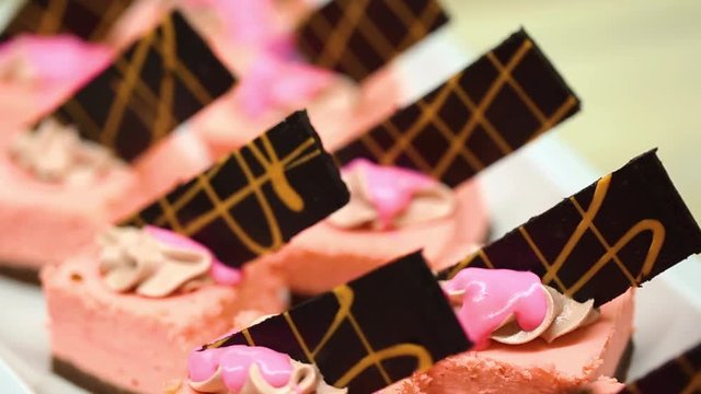 Closeup view of many small pink cakes served on table for cocktail party or on shelves at store.