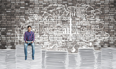 Attractive man sitting on pile of paper documents.