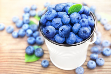 Bucket of fresh ripe sweet juicy blueberries with leaves on wooden background, selective focus, toned