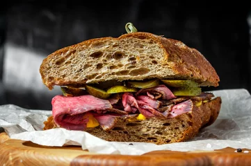 Fotobehang Broodje Pastrami op roggebrood met augurk en mosterdsaus, geserveerd op houten bord © maxpetrov