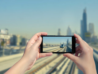 Female's hands take a picture of Dubai monorail and skyscrapers on mobile phone. Picture of subway...