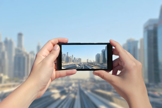 Female's hands take a picture of Dubai monorail and skyscrapers on mobile phone. Picture of subway road on downtown city Dubai on smartphone. United Arab Emirates