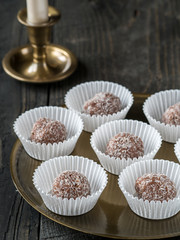 Homemade coconut and chocolate balls in white paper cupcakes on golden tray and wooden table.