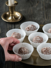 Homemade coconut and chocolate balls in white paper cupcakes on golden tray and wooden table.