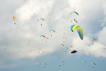 Paragliding in the blue sunny sky. Group of paragliders fly in summer sunny day in the Carpathians. Paragliders against the background of clouds.