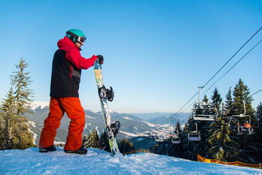 Male snowboarder resting with his snowboard on top of the mountain observing nature at ski resort on a beautiful sunny winter day, looking away copyspace ski lift active lifestyle sports Bukovel
