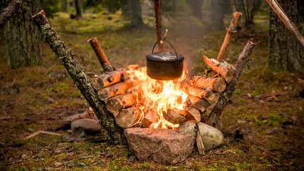 Pot hanging over an intense fire in a bushcraft setting.