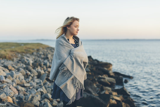 A young woman wrapped in a shawl looking out to sea
