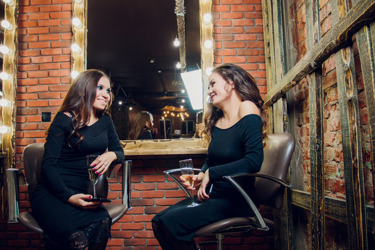 Two beautiful young woman outside at a city cafe laughing and drinking champagne