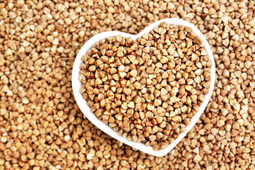 Heart shaped bowl of roasted buckwheat on buckwheat groat background, gluten free ancient grain for healthy diet, selective focus