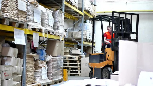 Forklift pallet with boxes in modern warehouse. Warehouse worker driver in uniform moving cardboard boxes by forklift stacker loader