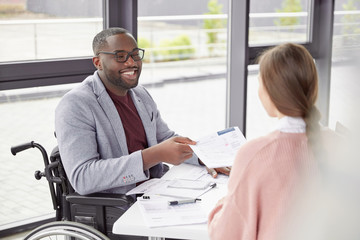 African American male invalid sits at workplace in wheelchair, shares creative ideas and opinions...