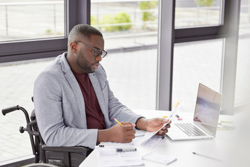 Portrait of dark skinned male invalid reviews contract before meeting with partners, sits in office...