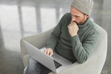 Top view of concetrated male copywriter in warm sweater and jeans involved in remote job, prepares...