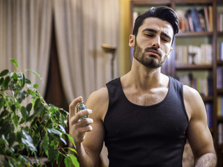 Handsome muscular young man in his home spraying cologne or perfume on neck