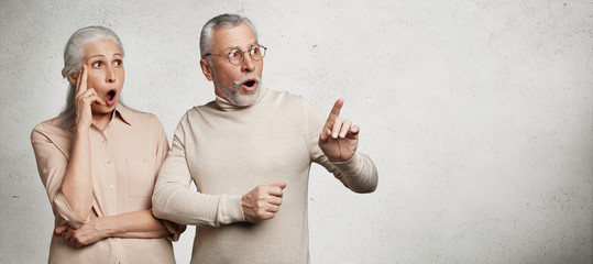 Shocked amazed senior grey haired old female and male dressed casually, indicate with great...