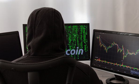 hacker in front of the monitors looking financial graphics of crypto coins