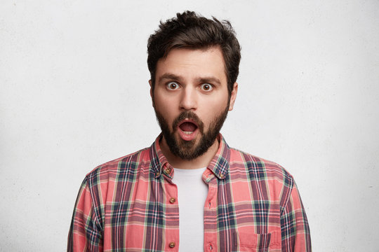 People, reaction and attitude concept. Emotional male with jaw dropped out, straes at camera, being stupefied to realize about his big failure or fault, isolated over white studio background