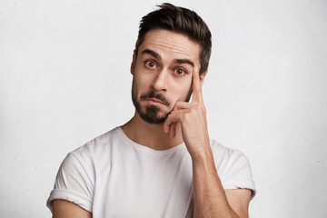 Attractive male with dark beard and mustache looks with wonderment as hears something unexpected,...