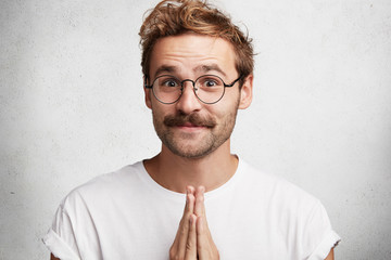 Funny bearded male with hands pressed together, looks innconetly, asks his girlfriend for...