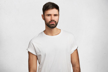 Waist up portrait of serious stylish attractive man with thick beard looks confidently, dressed in...