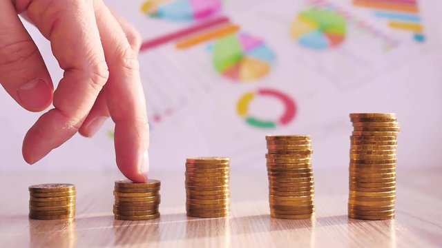 Man hand holding coin dollar on money coin stack arranged as a graph on wooden table. Hand of male or female finger step coins stack growing growth saving money. Business idea.