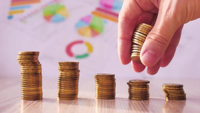 Man hand holding coin dollar on money coin stack arranged as a graph on wooden table. Hand of male or female finger step coins stack growing growth saving money. Business idea.