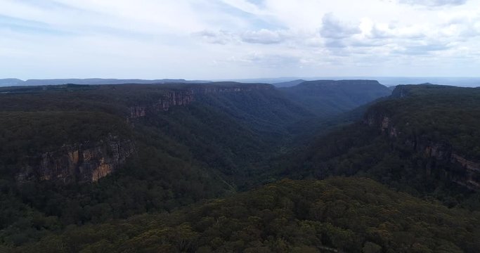 Morton national park along Yarrunga creek off Fitzroy falls flying forward over gum-tree woods and sandstone cliffs of the mountains.
