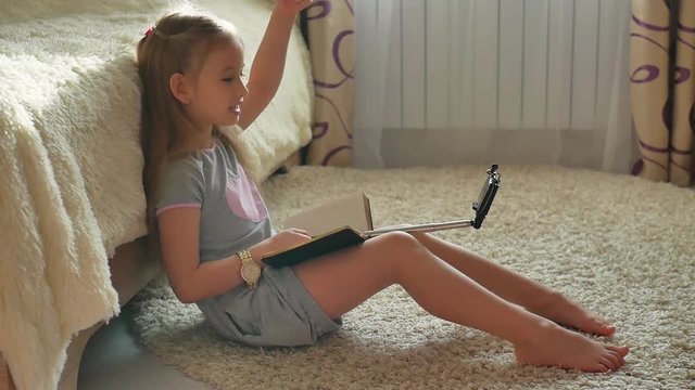 Happy little girl or blogger with camera mobile phone recording video and showing her drawings at home. Blogging, technology, videoblog, mass media and people concept.