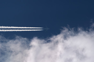 Passenger jet in flight above clouds, with contrails