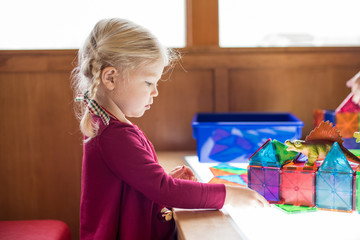 Little girl playing at light table with magnetic tiles