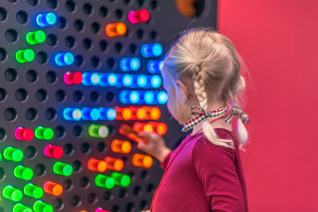 Little girl putting pegs in a light wall - hands on learning concept