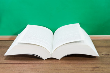 Open book on wooden desk with chalkboard.