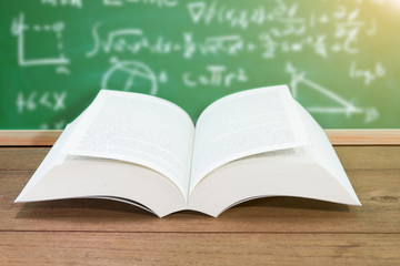 Open textbook on desk on chalkboard.