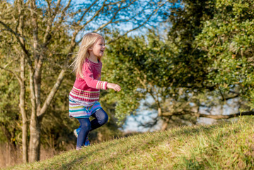Happy little girl running on grassy hill in the park, laughing, jumping