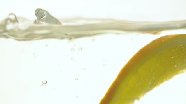 Orange slice falling into water on white background slow motion close up full hd video. Water surface with floating cutting citrus fruit, splash bubbles and waves