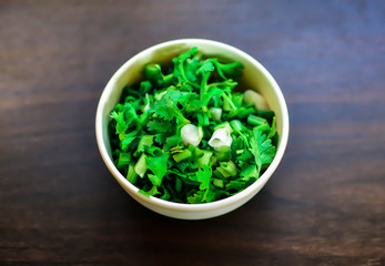 Bowl of chopped spring onions isolated on wood background, top view