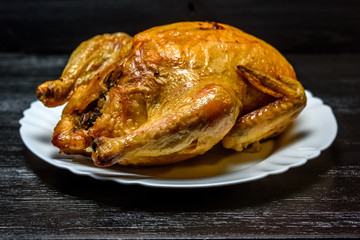 roast chicken on a white plate, on a black wooden background