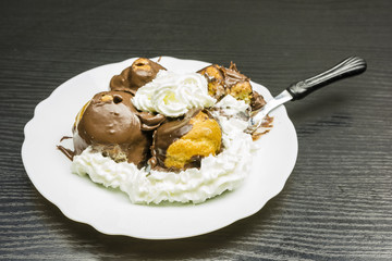 Fork with a portion of Profiterole with whipped cream.