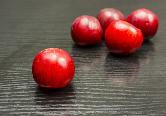 A ripe red plum, in a group of few plums on a wooden table.